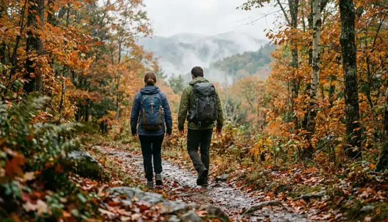 Two hikers walk a misty autumn trail, showing the best time to visit Gatlinburg for fall foliage