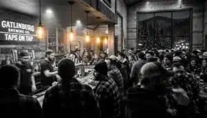 Crowded taproom scene on a brewery tours Gatlinburg stop, with silhouetted patrons and warm lights before a snowy mountain window