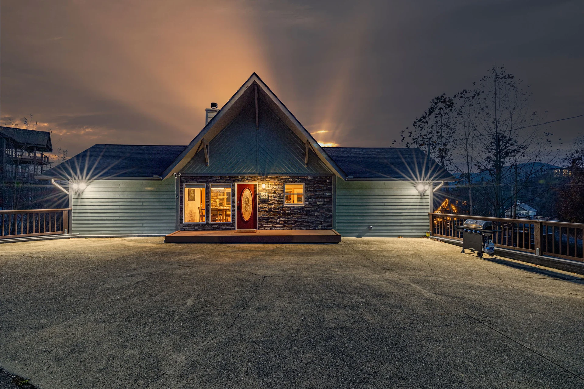 Twilight exterior of a stone-faced A-frame cabin with red door and wooden deck, a cabin deck with fire pit for a bachelor